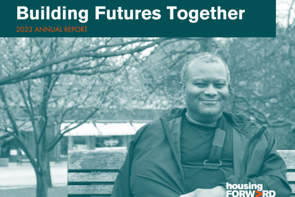 Duotone photograph shows a man sitting on a park bench and smiling.